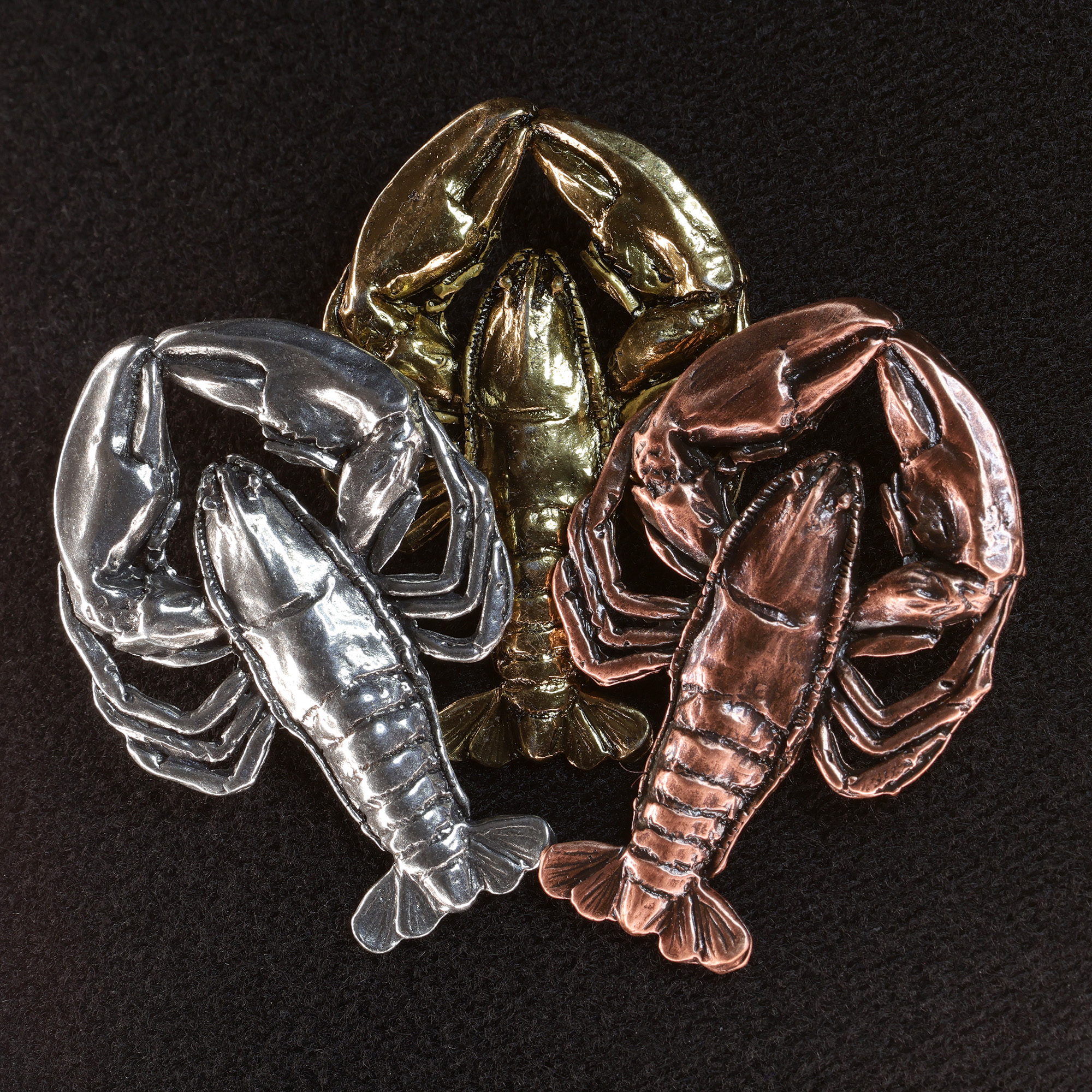 Three metal lobster castings in silver, gold, and copper